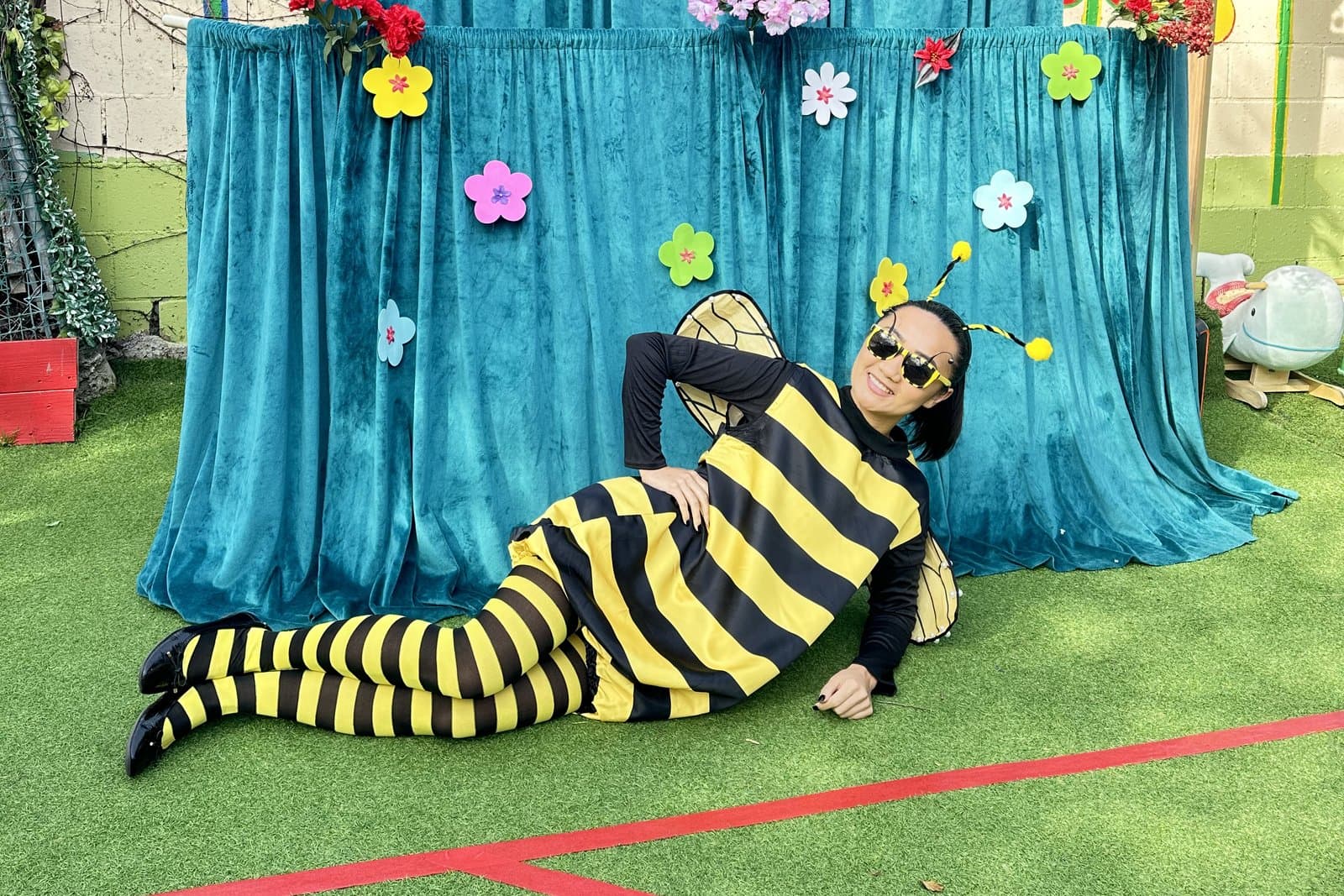 A performer in a bee costume on the grass in front of a flower-decorated backdrop.
